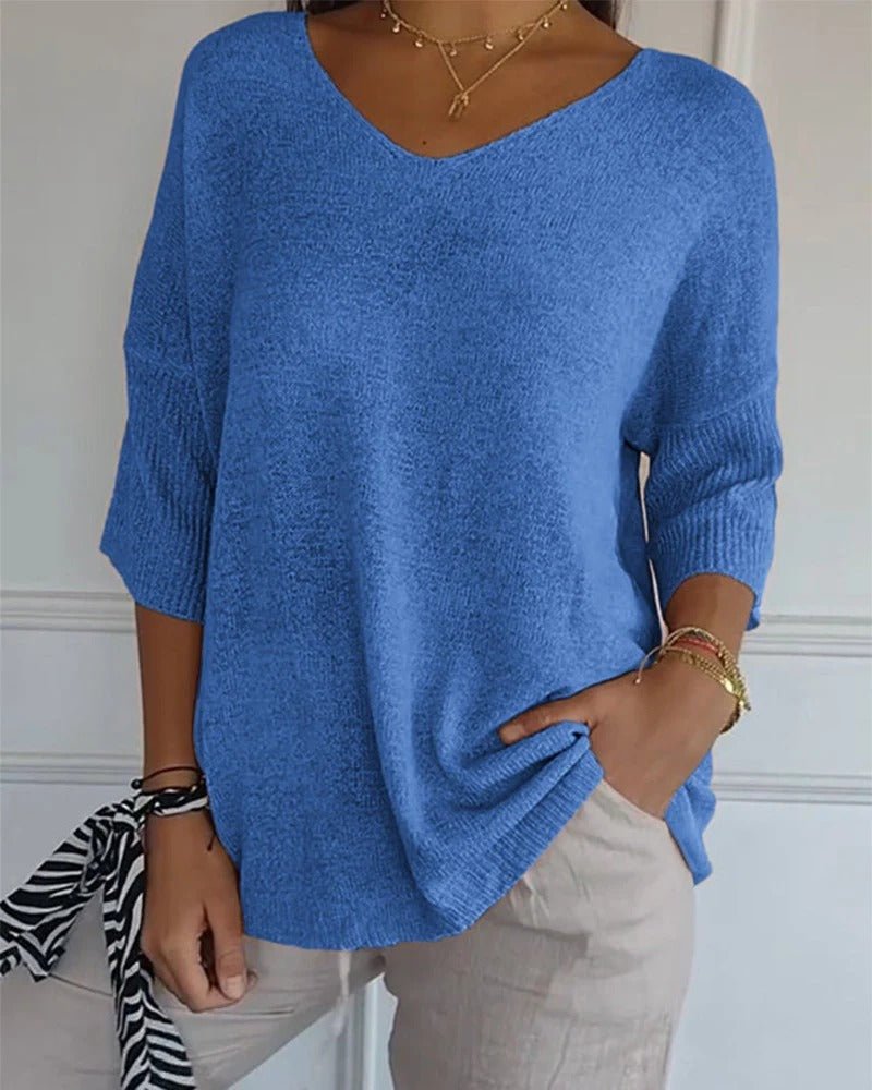 Model draagt blauwe pullover met V-hals en geribbelde mouwboorden, gecombineerd met beige broek en gouden kettingen 1