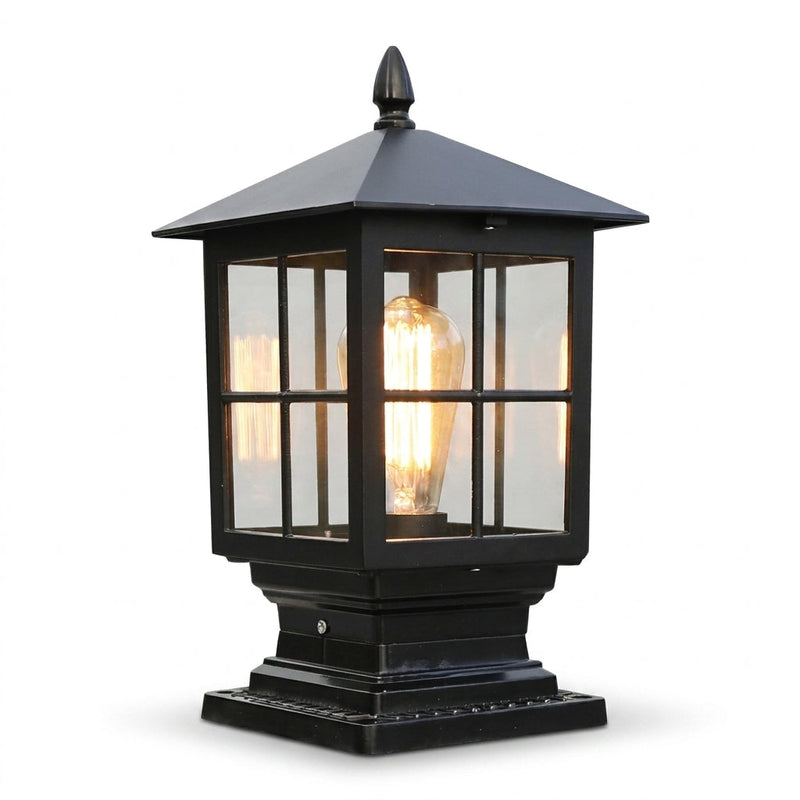 Zwarte pilaarlamp met ruitjesraam, spitse dakpunt en brandende gloeidraadlamp, vrijstaand tegen een witte achtergrond. 1