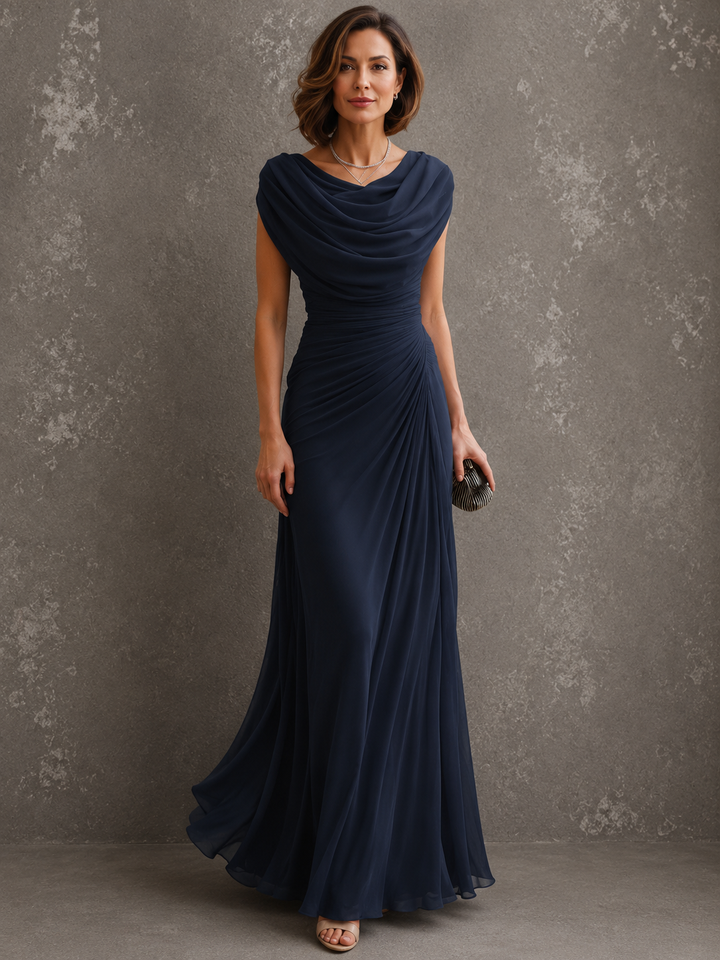 Model in dezelfde jurk in donkerblauw, vooraanzicht met gedrapeerde halslijn en vloerlange rok, clutch in de hand. 2