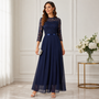 Model draagt de donkerblauwe jurk met kanten bovenstuk en vloeiende chiffon rok, met een zilverkleurig clutchtasje in de 2