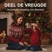 Meisje in rode trui houdt de acryl hanger met opgerold biljet omhoog, terwijl haar moeder lachend bij de kerstboom toekijkt. 3