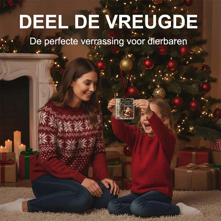 Meisje in rode trui houdt de acryl hanger met opgerold biljet omhoog, terwijl haar moeder lachend bij de kerstboom toekijkt. 3