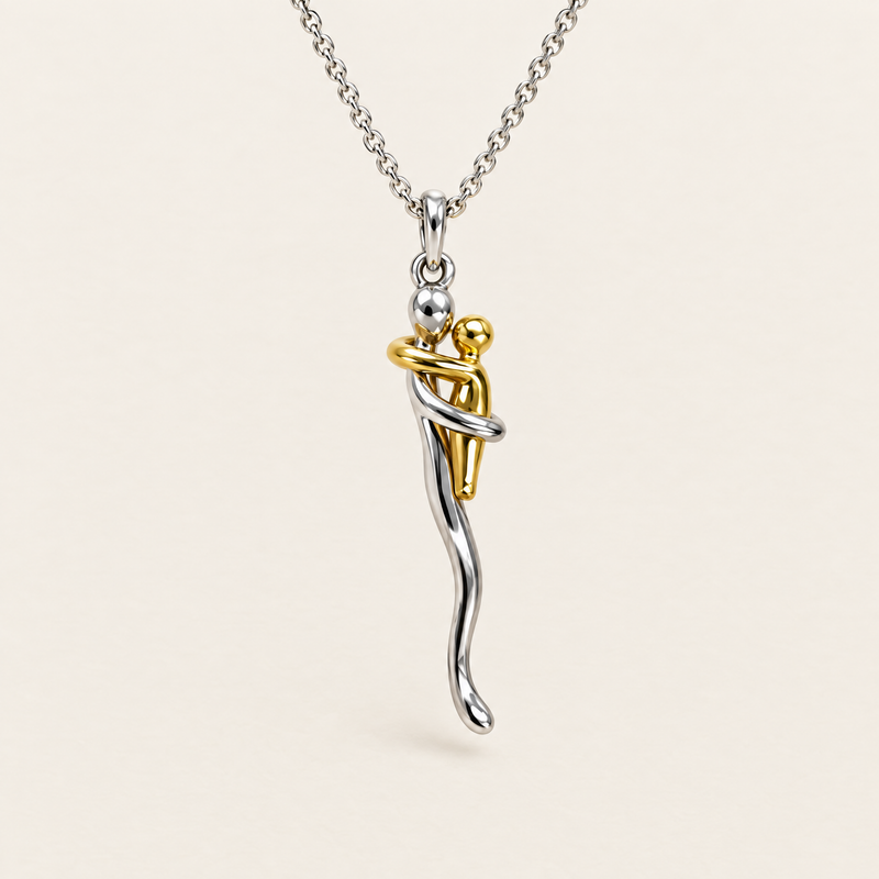 Zilverkleurige schakelketting met hanger van twee omhelzende figuurtjes, een zilverkleurig groot en een goudkleurig klein, vooraanzicht op een crèmekleurige ach 1