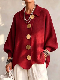 Model draagt het gebreide vest in rood met gouden knopen en een witte broek, vooraanzicht. 11