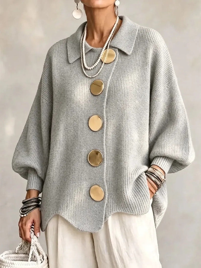 Model draagt het gebreide vest in lichtgrijs met gouden knopen en een witte broek, vooraanzicht. 10