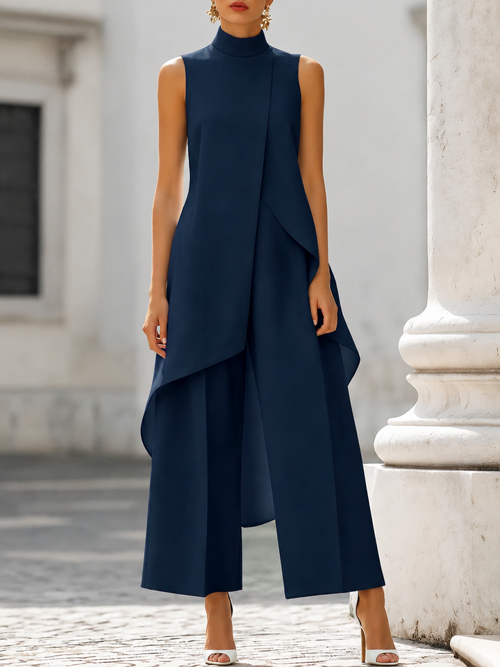 Marineblauwe set met asymmetrische top met opstaande kraag en wijde broek, gedragen door een model voor een witte zuil. 6
