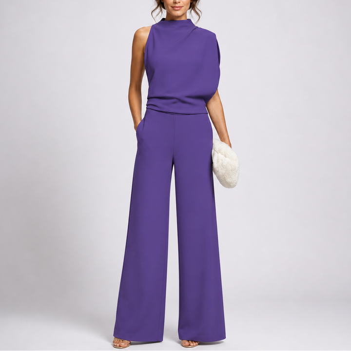 Model draagt de jumpsuit in paars met een asymmetrisch gedrapeerd bovenstuk en sandalen 3