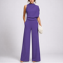 Model draagt de jumpsuit in paars met een asymmetrisch gedrapeerd bovenstuk en sandalen 3