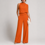 Model draagt de jumpsuit in oranje met wijde pijpen, een plooi bij de hals en nude pumps 5
