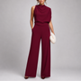 Model draagt de jumpsuit in bordeauxrood met gedrapeerd bovenstuk en wijde pijpen, met pluchen clutch 7