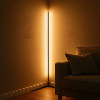 Dunne zwarte hoekvloerlamp die in een donkere kamer warm licht langs beide muren werpt, naast de armleuning van een bank. 3