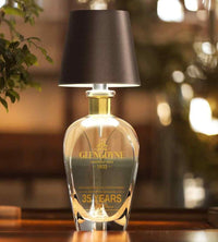 Donkerbruine lampenkap op een kristallen karaf met gouden hals, brandend op een houten tafel met plant. 5