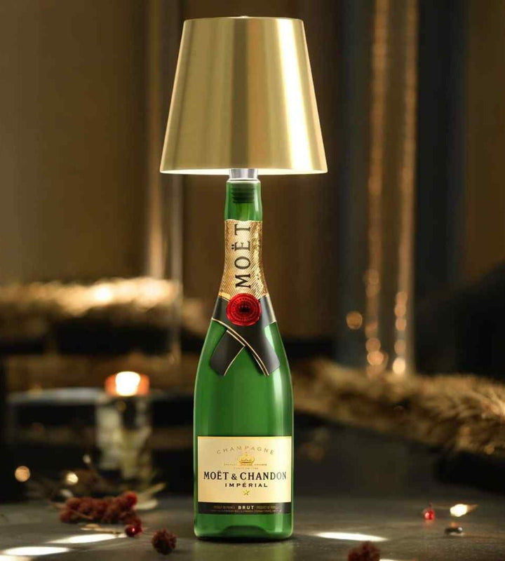Gouden lampenkap op een groene champagnefles, sfeervol verlicht op een tafel met kerstlichtjes en rode besjes. 1