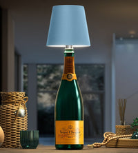 Lichtblauwe lampenkap op een groene champagnefles, omringd door rieten manden en kralen op een houten tafel. 6
