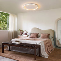 Ronde plafondlamp aan in een slaapkamer met bed in roze en witte tinten, houten bank, nachtkastje en grote spiegel. 11
