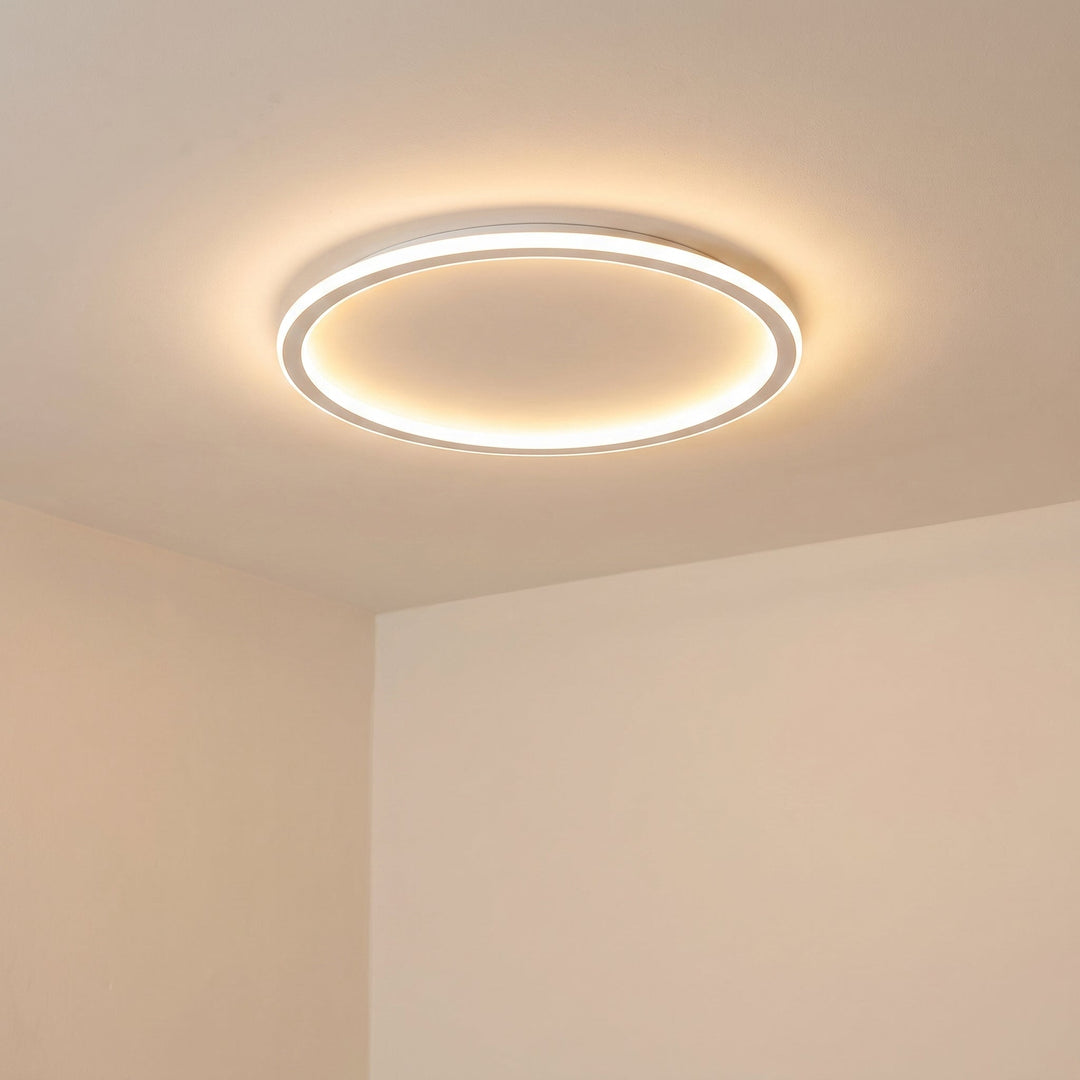 Aangezette witte ringlamp, schuin van onderaf gezien, die zacht licht over het crèmekleurige plafond en de muren verspreidt. 6