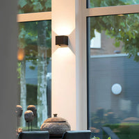 Zwarte wandlamp op een witte kolom naast grote ramen met uitzicht op een tuin 7