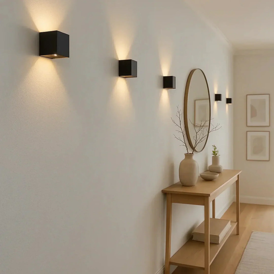 Rij zwarte kubuslampjes aan een lichte gangmuur boven een houten bijzettafel met vaas en ronde spiegel 3