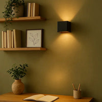 Zwarte wandlamp op een olijfgroene muur naast houten wandplanken met boeken, boven een bureau met notitieboek 9