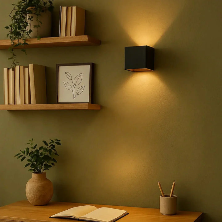 Zwarte wandlamp op een olijfgroene muur naast houten wandplanken met boeken, boven een bureau met notitieboek 9