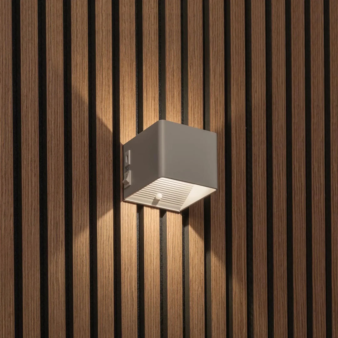 Lichte kubusvormige wandlamp op houten lamellenwand, schuin gezien met schakelaar en bewegingssensor onderaan 2