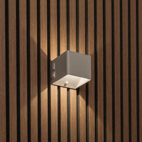 Lichte kubusvormige wandlamp op houten lamellenwand, schuin gezien met schakelaar en bewegingssensor onderaan 2