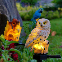 Verlichte witte uil in een tuin naast een oranje lichtgevend eekhoornbeeld en een blauwe papegaai. 12
