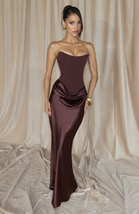 Model in de bruine korsetjurk voor beige gordijnen, met gouden armband en oorbellen 6