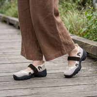 Beige schoenen met bruine klittenbandband en donkere zool, gedragen met een wijde bruine linnen broek op een houten loopbrug. 11