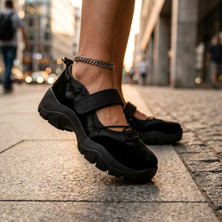 Zwarte schoenen met dikke zool en klittenbandband, gedragen met een enkelbandje op een stoep in de stad, close-up van opzij. 13