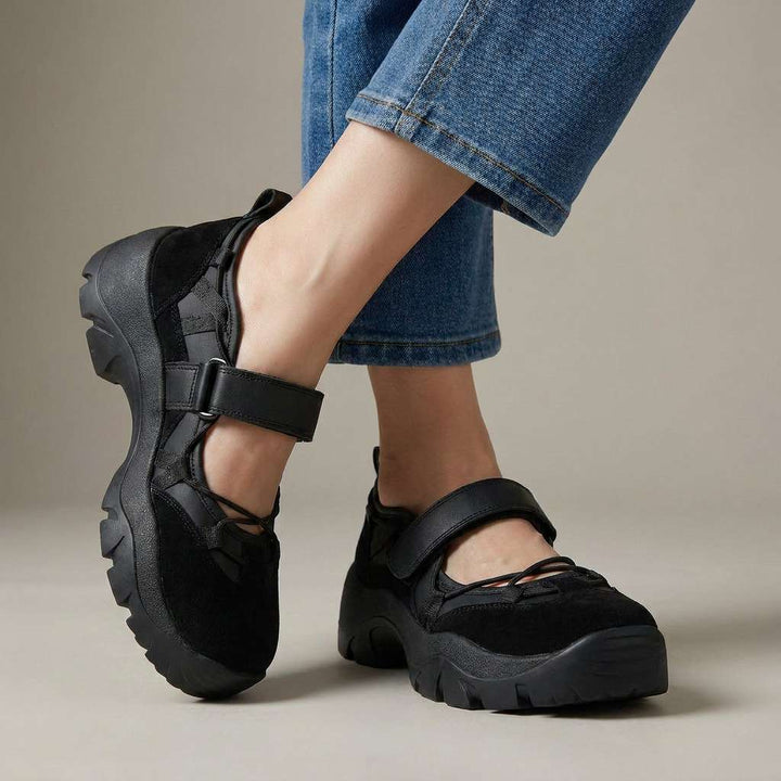 Zwarte schoenen met klittenbandband en dikke zwarte zool, gedragen met lichtblauwe jeans voor een neutrale studioachtergrond. 5