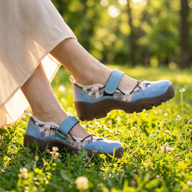 Blauwe suÃ¨de schoenen met ruitjesstof en bruine zool, gedragen met een lange beige rok in een zonnig grasveld. 8