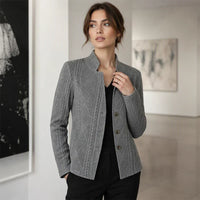 Vrouw in een galerie in een grijze blazer met kabelstructuur, zwarte top en zwarte broek, hand bij de kraag. 11