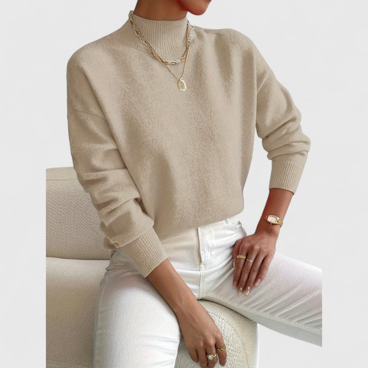 Model draagt de trui in beige met ribkraag en ribboorden, gecombineerd met witte broek, gouden kettingen en horloge. 7