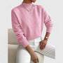 Model draagt de roze trui met ribkraag, lange mouwen en ribboorden, gecombineerd met witte broek en zilveren kettingen. 5