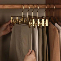 Hand pakt een broek van een rij goudkleurige hangers met klemmen in een houten kast 7