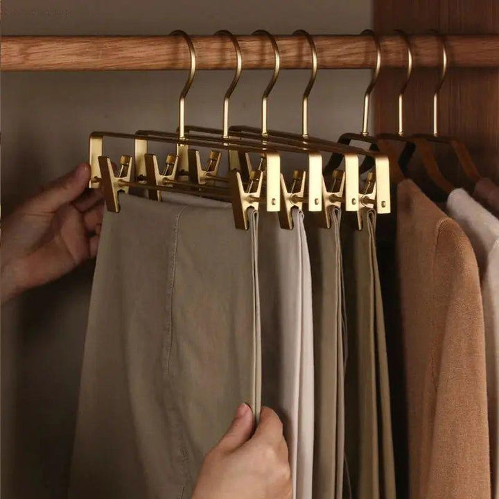 Hand pakt een broek van een rij goudkleurige hangers met klemmen in een houten kast 7