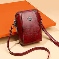 Donkerrode leren crossbodytas met sierstuk en lange band, schuin gefotografeerd voor een oranje vlak 7