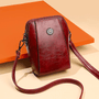 Donkerrode leren crossbodytas met sierstuk en lange band, schuin gefotografeerd voor een oranje vlak 7