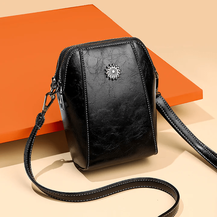 Zwarte leren crossbodytas schuin van voren op beige ondergrond met oranje achtergrondvlak 6