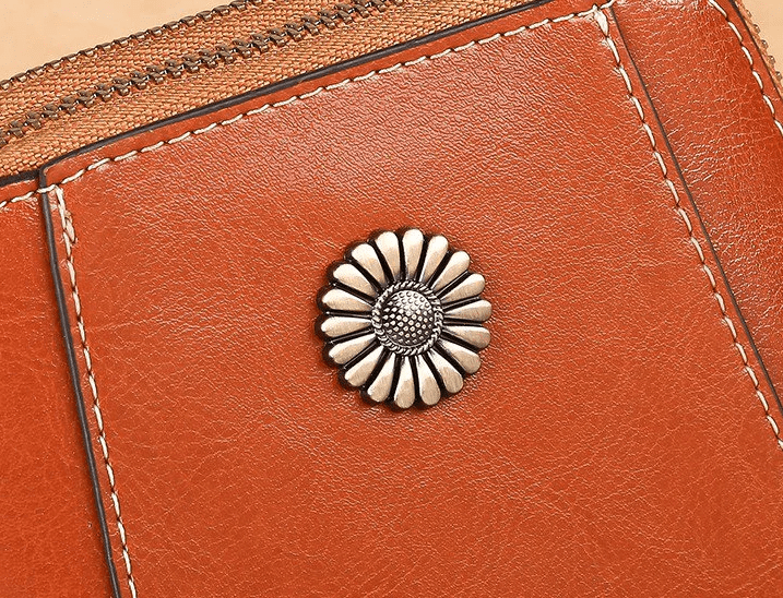 Close-up van het bloemvormige metalen sierstuk op roodbruin leer met lichte stiksels 4
