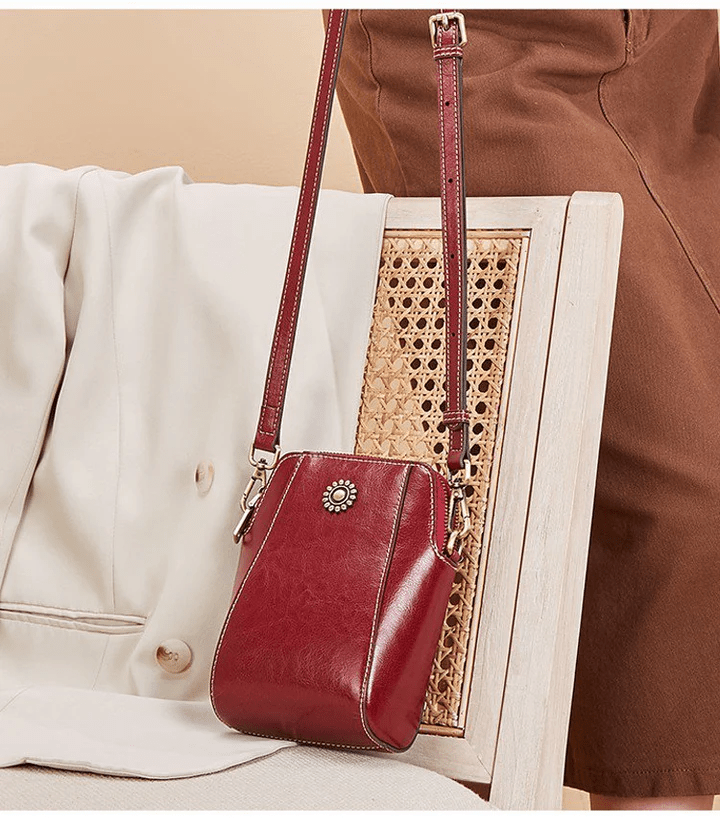 Rode leren tas met lange band hangend aan een rieten stoel naast een beige jasje 5