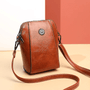 Roodbruine leren crossbodytas schuin van voren, met bloemvormig sierstuk en lange band op beige ondergrond 1