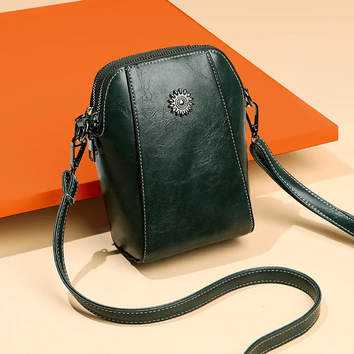 Donkergroene leren crossbodytas met bloemvormig sierstuk en lange band, schuin gefotografeerd voor een oranje vlak 8