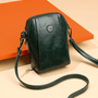 Donkergroene leren crossbodytas met bloemvormig sierstuk en lange band, schuin gefotografeerd voor een oranje vlak 8