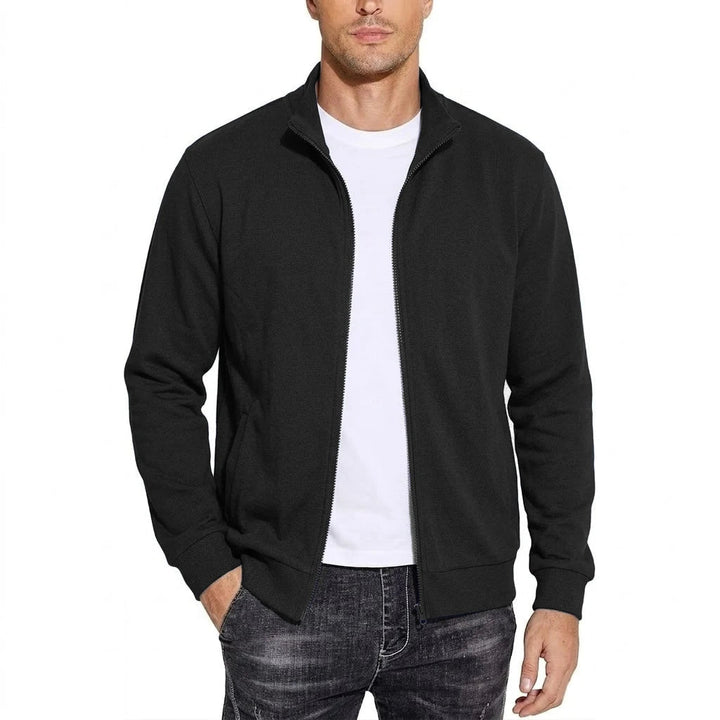 Model draagt de zwarte sweatshirtjack open over een wit T-shirt, met opstaande kraag, ribboorden en één hand in de zak. 1