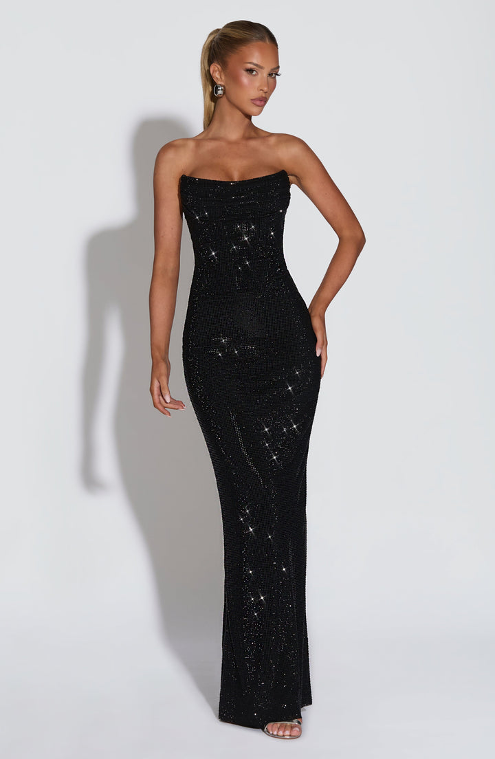 Vooraanzicht van de zwarte strapless maxi-jurk met strass op een model, hand op de heup, strakke pasvorm tot op de vloer. 22