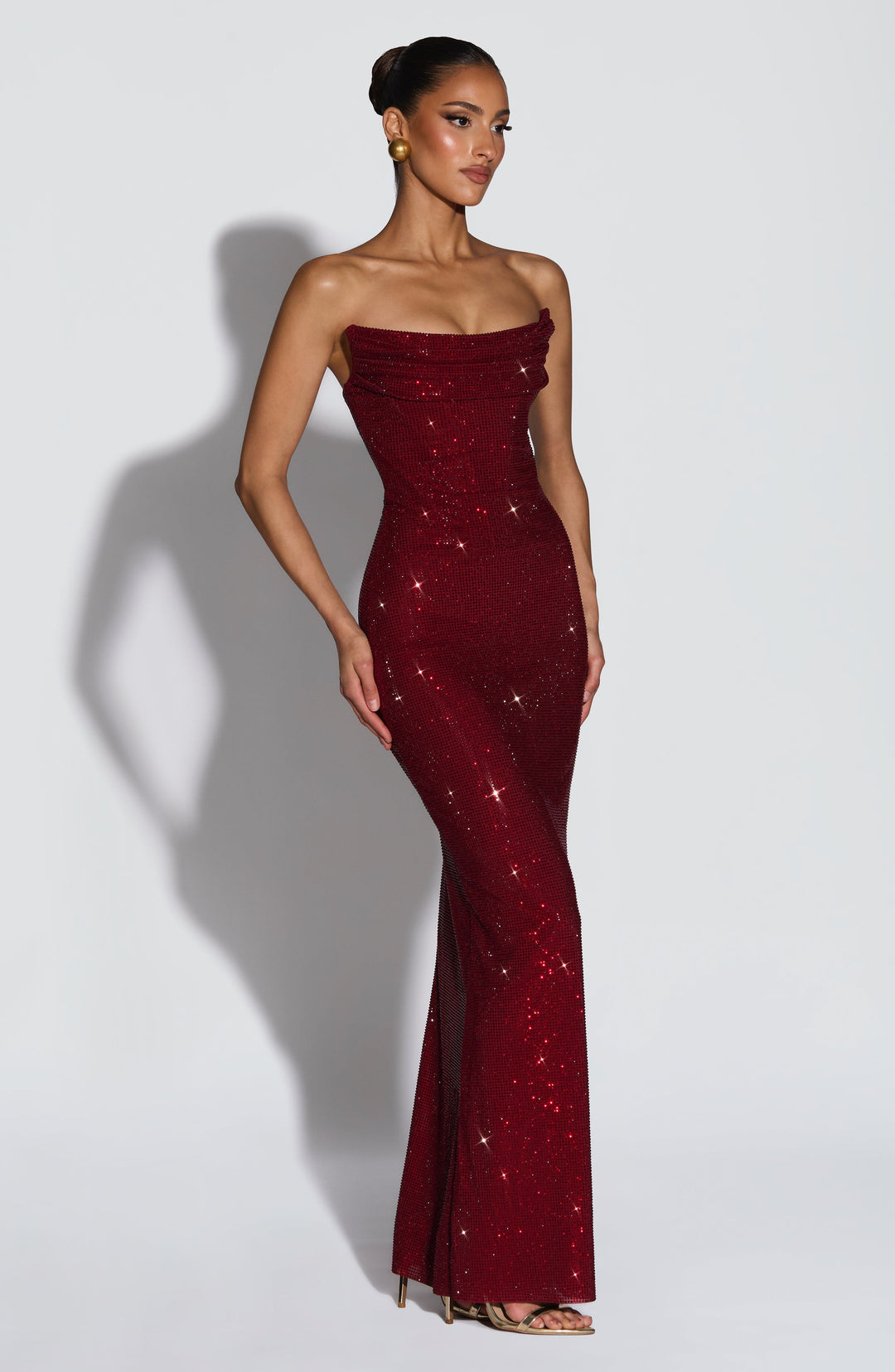 Model draait driekwart in de bordeauxrode strass-jurk, die het silhouet met lange rok laat zien. 4