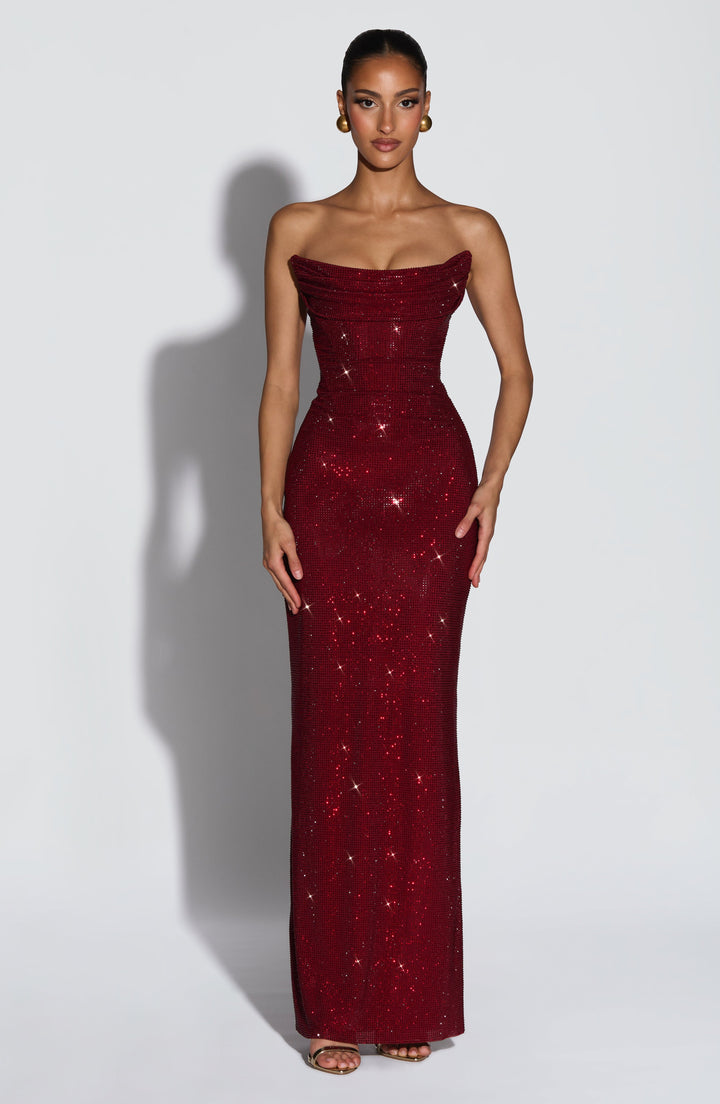 Model in bordeauxrode, glinsterende straploze maxi-jurk met drapering aan het lijfje, van voren gezien. 1
