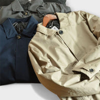 Drie jassen in beige, marineblauw en grijs naast elkaar gelegd, met omgeslagen kraag en knopen zichtbaar. 9
